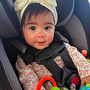 Persephone joined the competition — help win amazing prizes! baby, child, infant, car_seat, car, safety_harness, bow_headband, floral_clothing, toy, colorful_toys, portrait, close_up, wide_eyes, smiling, sitting, indoors, vehicle, parenting, cute, face