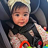 baby, child, infant, car_seat, car, safety_harness, bow_headband, floral_clothing, toy, colorful_toys, portrait, close_up, wide_eyes, smiling, sitting, indoors, vehicle, parenting, cute, face