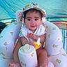 Persephone is registered to the contest to win money with this photo: baby, child, infant, portrait, sitting, smiling, sun_hat, colorful_clothing, high_chair, inflatable_chair, bottle, outdoor, tent, blue_background, teddy_bears, bare_feet, hands, happy, close_up, photography