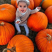 Persephone joined the competition — help win amazing prizes! baby, child, infant, smiling, happy, pumpkin, pumpkin_patch, halloween, outdoor, autumn, fall, nature, grass, portrait, sitting, baby_clothing, knit_hat, bonnet, orange, harvest