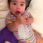 Persephone is registered to the contest to win money with this photo: baby, infant, child, face, portrait, smiling, surprised, awake, bottle, feeding, milk, striped_outfit, rainbow_colors, pajamas, pillows, blanket, indoors, couch, sitting, closeup