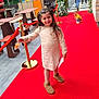 Angel a rejoint le concours — aidez-le/la à gagner de superbes lots ! child, girl, red_carpet, outdoor, smiling, boots, dress, snack, paper, greenery, decorations, people, adult, walking, pavement, fence, table, chair, daylight, event