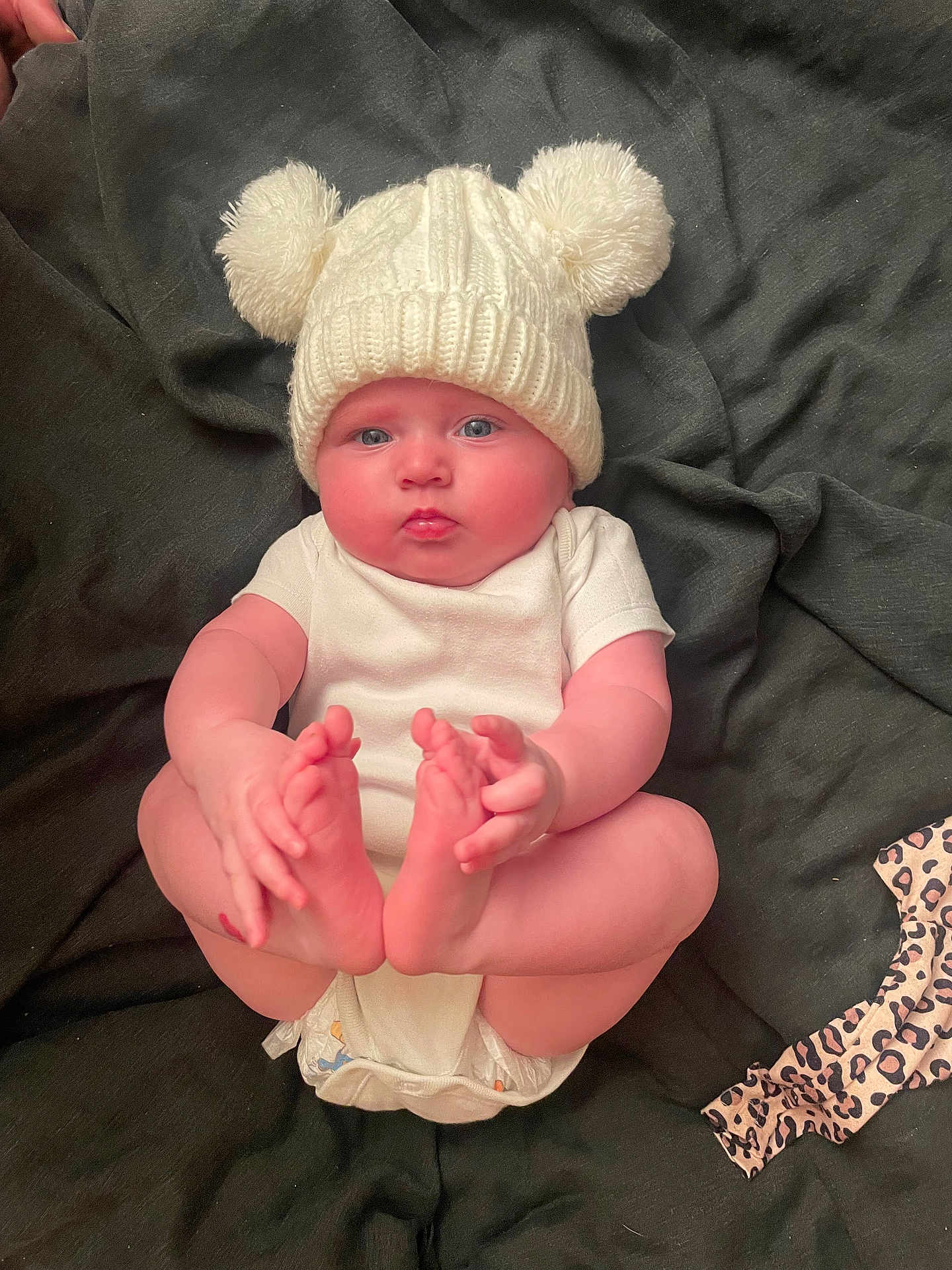 Delilah is registered to the contest to win money with this photo: baby, infant, hat, knit_hat, pom_poms, white_clothing, diaper, hands, feet, blue_eyes, blanket, lying_down, cute, chubby_cheeks, indoor, soft_texture, child, person, portrait, curious