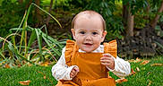 Aurora is registered to the contest to win money with this photo: autumn_leaves, baby, barefoot, child, cute, daylight, fall, garden, grass, greenery, happy, nature, orange_dress, outdoor, person, portrait, sitting, smiling, trees, young_child
