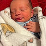 Luca is registered to the contest to win money with this photo: newborn, baby, sleeping, blanket, swaddled, heart_pattern, red_blanket, infant, cozy, soft_texture, cute, peaceful, hand, face, skin, indoors, portrait, resting, warm, comfort