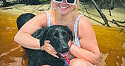 Retta joined the competition — help win amazing prizes! woman, dog, water, sunglasses, cap, smile, outdoor, nature, tree_roots, riverbank, summer, pet, black_dog, happy, sitting, swimsuit, sunny, playful, friendship, relaxation