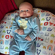 William is registered to the contest to win money with this photo: baby, infant, blue_clothing, giraffe_applique, pillow, animal_print, smile, face, child, cozy, socks, seated, indoor, cute, person, home, furniture, patterned, comfort, soft