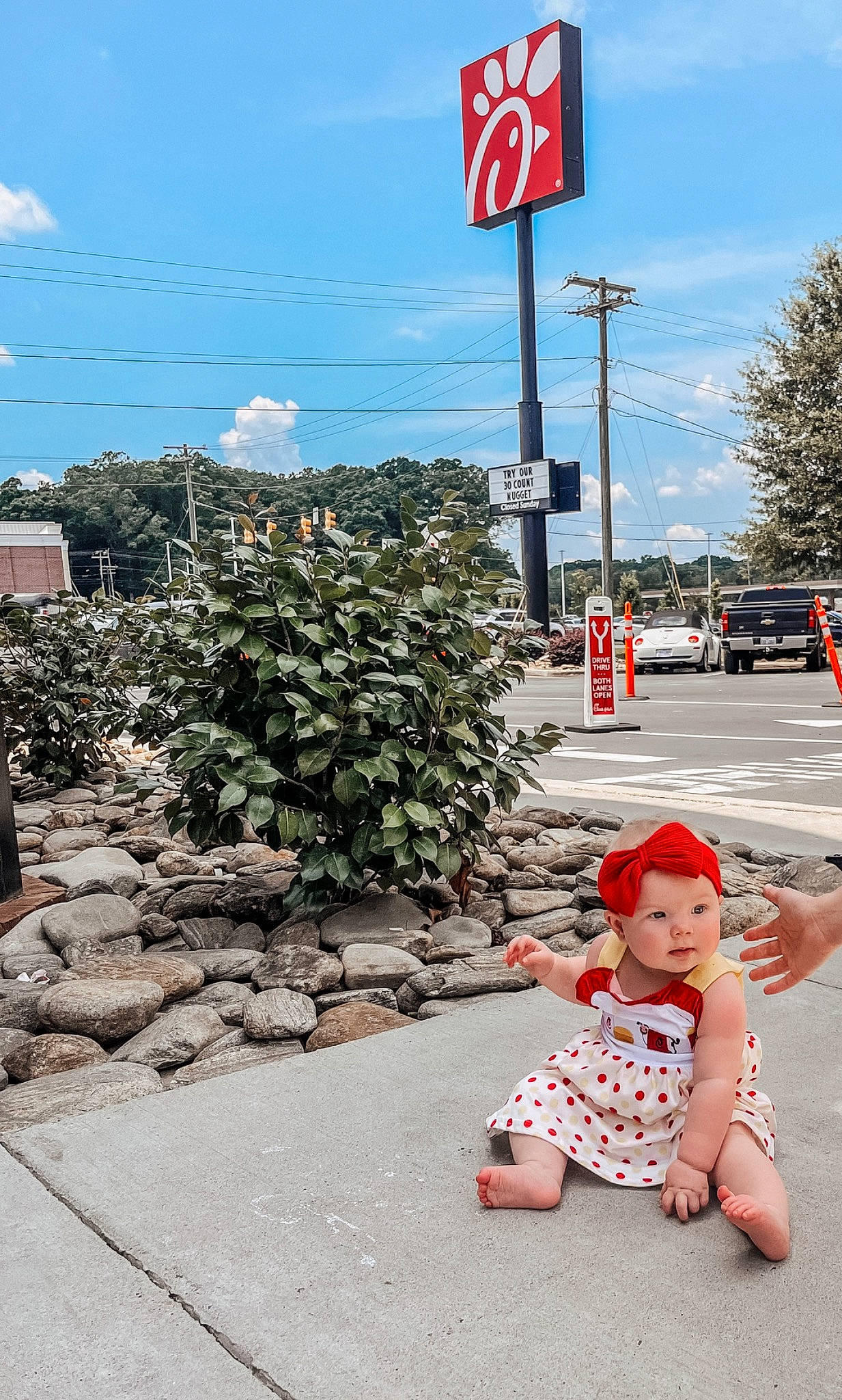 Nora is registered to the contest to win money with this photo: asphalt, baby, baby_toddler_clothing, city, cloud, flooring, headwear, infrastructure, line, person, plant, public_space, red, road, road_surface, sidewalk, sky, street, summer, toddler