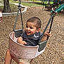 Jireh is registered to the contest to win money with this photo: child, toddler, swing, playground, smiling, outdoor, wood_chips, clothing, shorts, shirt, metal, chains, happy, person, park, trees, slide, bench, daytime, fun