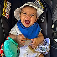 Jireh is registered to the contest to win money with this photo: baby, child, car_seat, hat, blue_bib, plush_toy, blanket, smiling, happy, infant, sitting, toy, clothing, face, person, safety_warning, indoor, cute, headwear, closeup