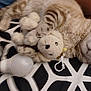 cat, plush_toy, stuffed_animal, light_bulb, blanket, pattern, striped, fur, pet, cozy, resting, soft, indoor, animal, sleeping, cute, home, comfort, claw, paw
