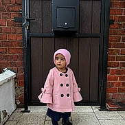 Inayah is registered to the contest to win money with this photo: child, pink_coat, pink_hat, black_shoes, brick_wall, wooden_door, mailbox, outdoor, pavement, side_view, standing, curious, winter_clothing, young_child, portrait, daylight, urban, casual, fashion, person