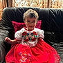 child, toddler, smiling, red_dress, white_top, embroidery, sitting, couch, leather_couch, cushion, curtains, indoors, natural_light, happy, person, face, hair, fabric, pattern, furniture