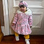toddler, child, pink_coat, hat, yellow_pants, white_sneakers, indoor, wooden_floor, door, fashion, winter_clothing, standing, cute, portrait, young_child, warm_clothing, person, floor, white_door, fur_trim