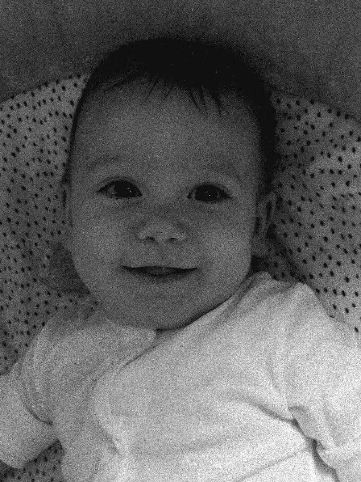 Anakin is registered to the contest to win money with this photo: baby, infant, smiling, face, portrait, black_and_white, clothing, onesie, lying_down, blanket, polka_dot, head, hair, cute, happy, child, person, close_up, indoors, young