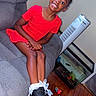 Rhyder is registered to the contest to win money with this photo: child, girl, smiling, red_dress, boots, socks, couch, indoor, wooden_floor, fish_tank, fan, happy, seated, home, furniture, portrait, black_hair, casual, playful, person