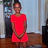 Rhyder joined the competition — help win amazing prizes! child, girl, red_dress, glasses, smiling, standing, indoor, carpet, wooden_floor, plant, shelf, door, black_boots, hair_bun, home, furniture, happy, portrait, person, casual