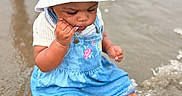 Skhylar joined the competition — help win amazing prizes! toddler, child, water, beach, sand, bucket_hat, denim_dress, water_splash, barefoot, playing, outdoor, summer, person, legs, toy_bucket, reflection, sitting, casual_clothing, cute, curious