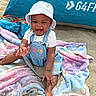 Skhylar is registered to the contest to win money with this photo: baby, child, smiling, happy, beach, sand, blanket, pastel_colors, denim_overalls, bucket_hat, outdoor, sunny, tent, playful, sandy_hands, infant, casual_clothing, summer, cute, portrait