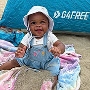 Skhylar is registered to the contest to win money with this photo: baby, child, beach, sand, blanket, hat, denim_overalls, smiling, happy, outdoor, sun_hat, toddler, colorful_blanket, playful, summer, tent, sitting, portrait, cute, sunny