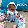 baby, child, beach, sand, blanket, hat, denim_overalls, smiling, happy, outdoor, sun_hat, toddler, colorful_blanket, playful, summer, tent, sitting, portrait, cute, sunny