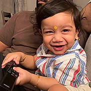 Narayan joined the competition — help win amazing prizes! child, toddler, smile, remote_control, striped_shirt, shorts, bracelet, earrings, forehead_mark, adult, beard, glasses, sofa, indoor, family, portrait, happy, sitting, close_up, cute