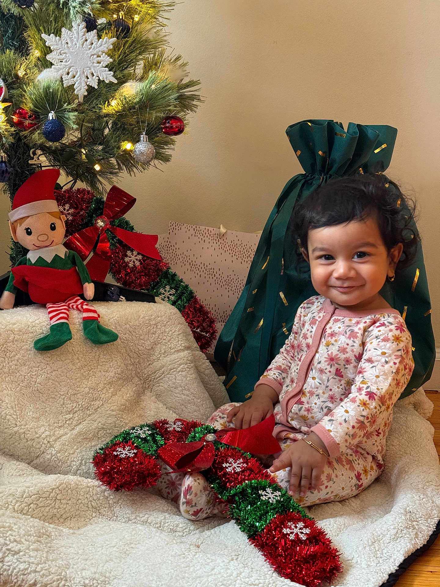 Narayan joined the competition — help win amazing prizes! toddler, child, smile, christmas_tree, ornament, snowflake_ornament, stuffed_elf, plush_toy, garland, ribbon, gift_bag, present, blanket, pajamas, cozy, festive, holiday, portrait, earring, wooden_floor