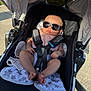 baby, stroller, sunglasses, infant, child, sunlight, blanket, safety_harness, outdoor, footwear, baby_clothing, cute, relaxing, summer, shade, accessory, portrait, seat, baby_bib, legs
