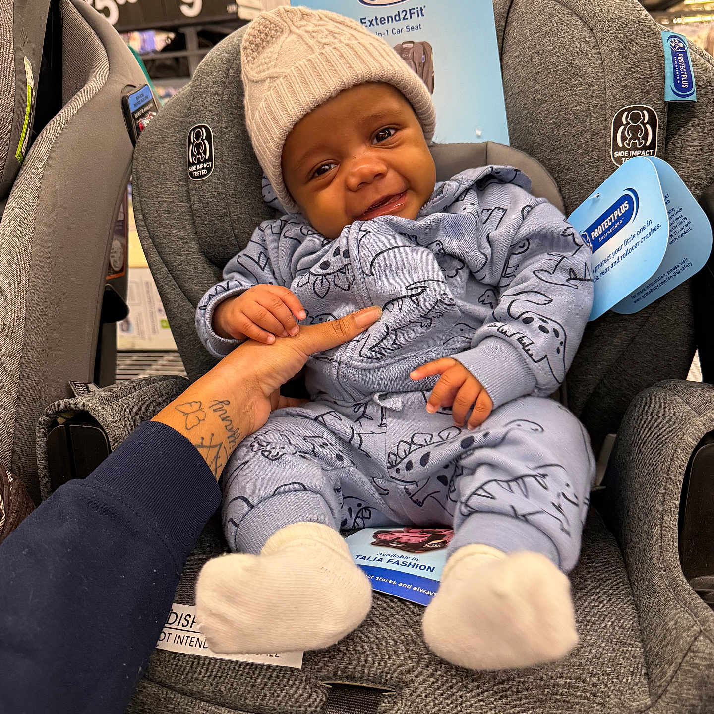 Zackaron joined the competition — help win amazing prizes! baby, car_seat, child, clothing, cute, dinosaur_pattern, display, gray, hand, hat, holding, indoor, infant, knit_hat, person, price_tag, product_label, smile, socks, store