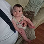 baby, child, infant, person, face, smile, food, mouth, arm, leg, hand, couch, pillow, clothing, indoor, floor, wood_floor, adult, holding, casual