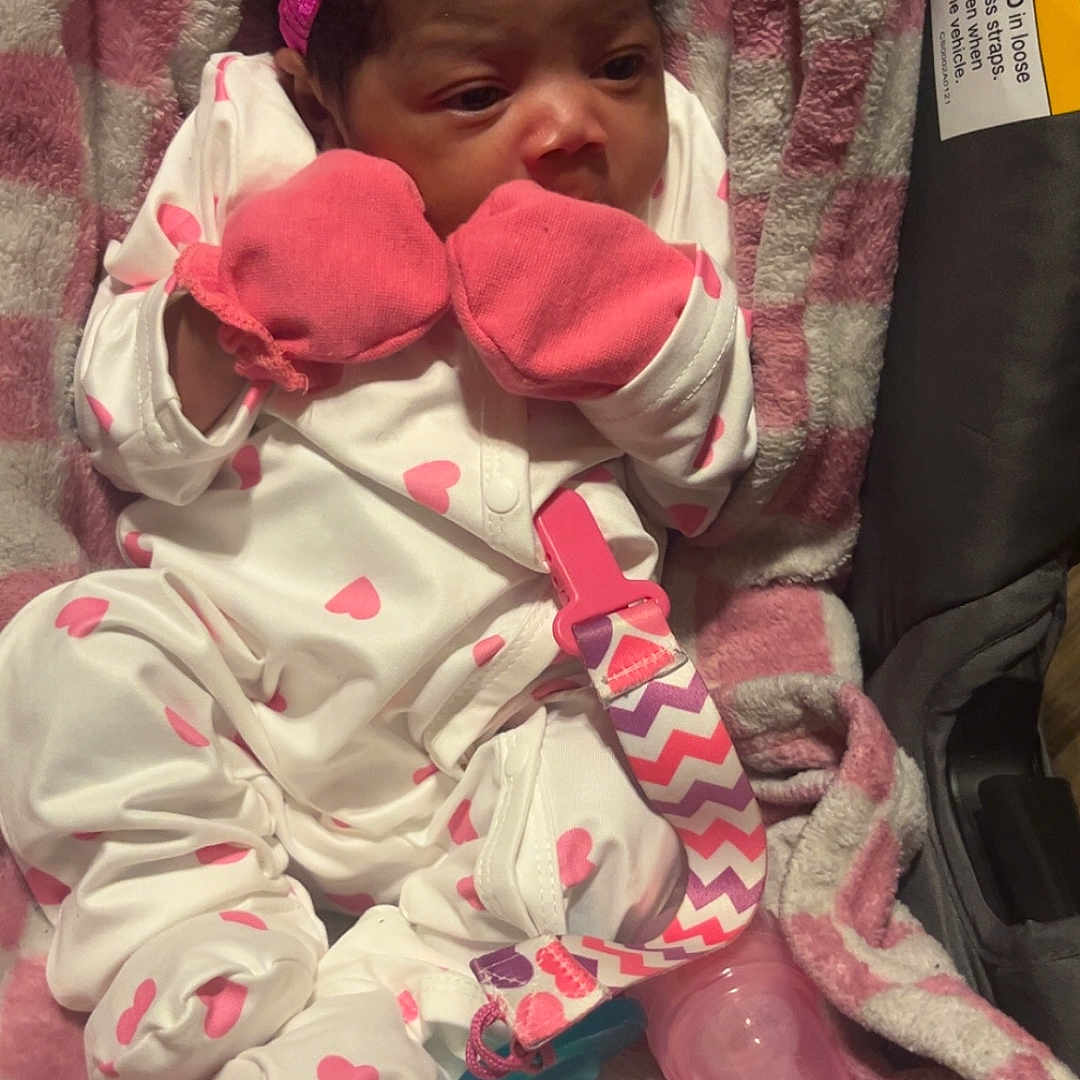 Diyara is registered to the contest to win money with this photo: accessory, baby, blanket, bottle, car_seat, checkered, child, cozy, cute, headband, indoor, infant, lying_down, mittens, newborn, onesie, pacifier, pink, sleepwear, soft