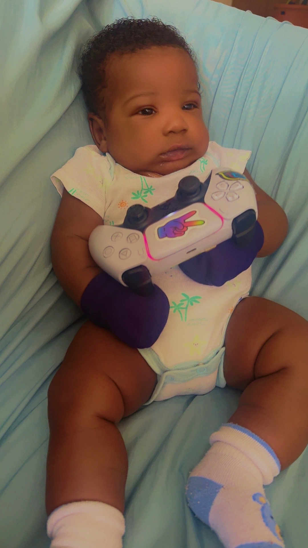 Arthur Chery is registered to the contest to win money with this photo: baby, blue_blanket, child, chubby_legs, closeup, curious, cute, expression, feet, gaming_controller, hands, indoor, infant, mittens, onesie, portrait, relaxed, seated, socks, soft_lighting