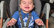 Robin is registered to the contest to win money with this photo: baby, high_chair, blue_clothing, smiling, happy, indoor, living_room, television, furniture, child, seat_belt, arms, legs, carpet, wall_art, wood_floor, person, portrait, cute, toddler