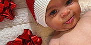 Ayla joined the competition — help win amazing prizes! baby, blanket, cheeks, cute, face, festive, hand, happy, holiday, holiday_decor, infant, knit_hat, lying_down, portrait, red_gift_bows, red_hat, skin, smiling, soft_texture, white_bow