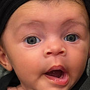 Ayla is registered to the contest to win money with this photo: baby, close_up, face, headband, black_clothing, expression, wide_eyes, mouth_open, infant, cute, child, skin, person, portrait, young, curious, headwear, indoors, human, newborn