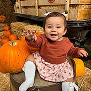Melissa is registered to the contest to win money with this photo: baby, child, smiling, happy, pumpkin, pumpkin_patch, autumn, fall, hay_bale, barrel, rustic, outdoor, portrait, sitting, reaching, dress, sweater, white_socks, hair_bows, farm_scene