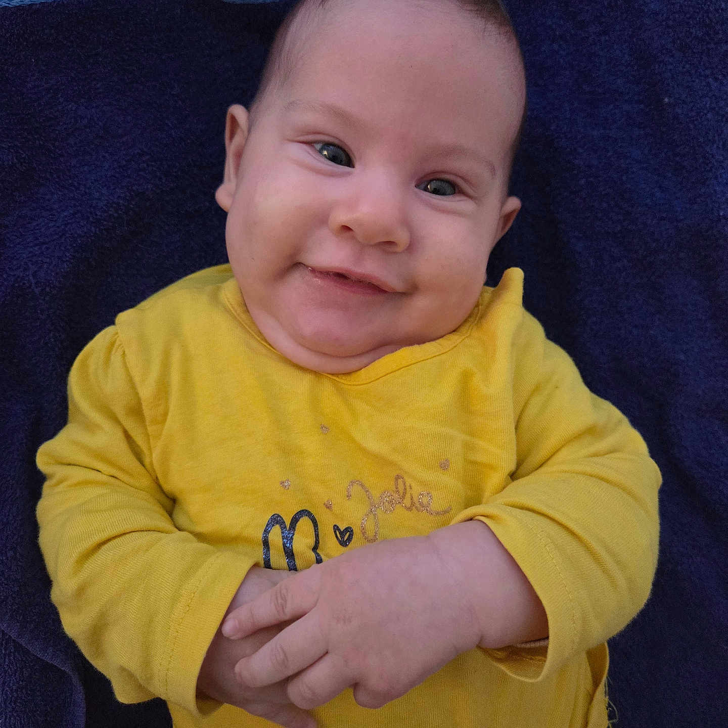 Célia a rejoint le concours — aidez-le/la à gagner de superbes lots ! baby, casual_clothing, child, closeup, cute, expression, eyes, face, hands, happy, indoors, infant, lying_down, person, portrait, skin, smiling, towel, yellow_shirt, young