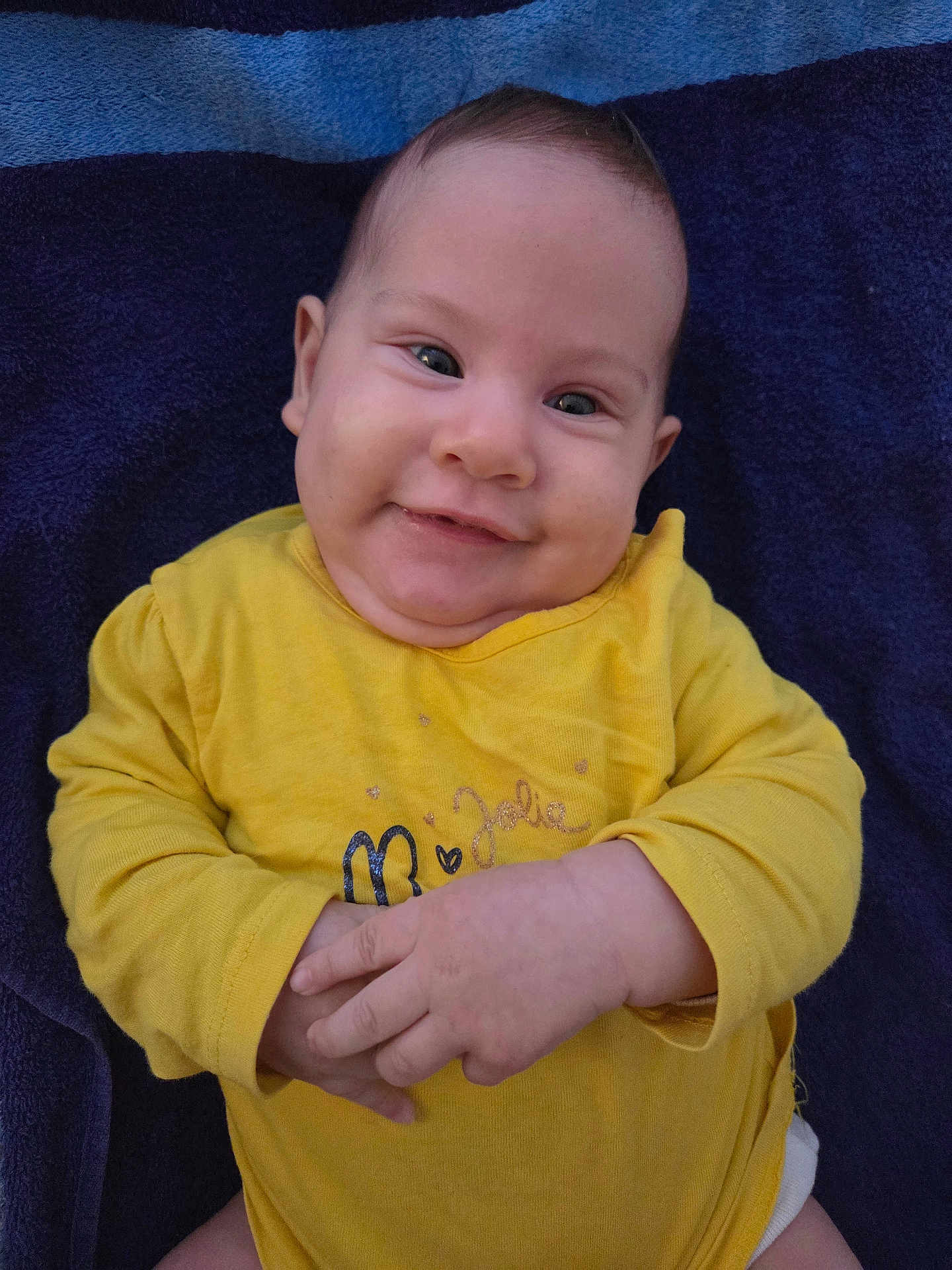 Célia a rejoint le concours — aidez-le/la à gagner de superbes lots ! baby, infant, smiling, yellow_shirt, towel, hands, face, cute, child, portrait, skin, eyes, expression, lying_down, indoors, closeup, person, happy, young, casual_clothing
