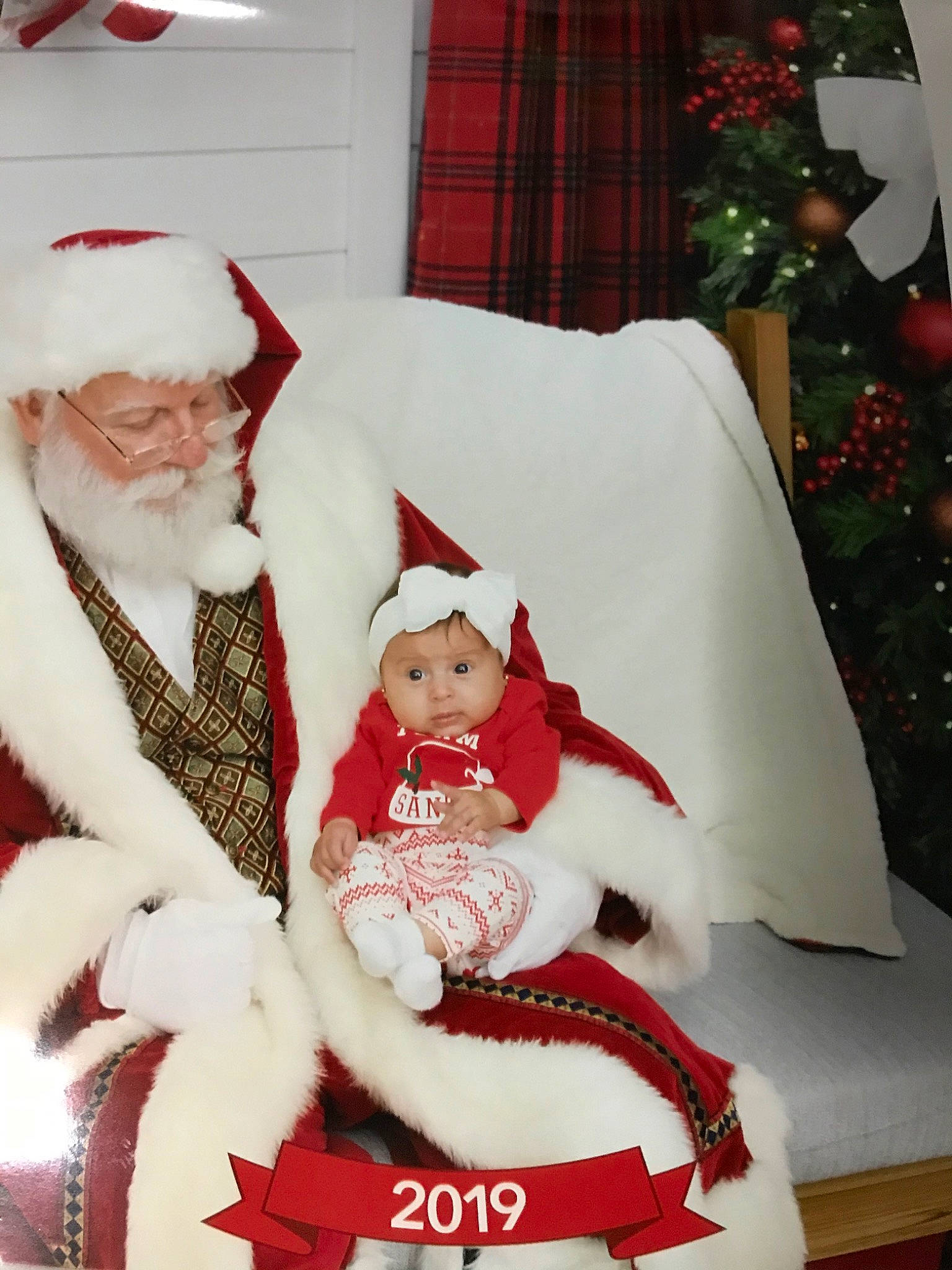 Aliana is registered to the contest to win money with this photo: carmine, child, christmas, christmas_eve, event, fictional_character, headwear, holiday, holiday_ornament, lap, person, santa_claus