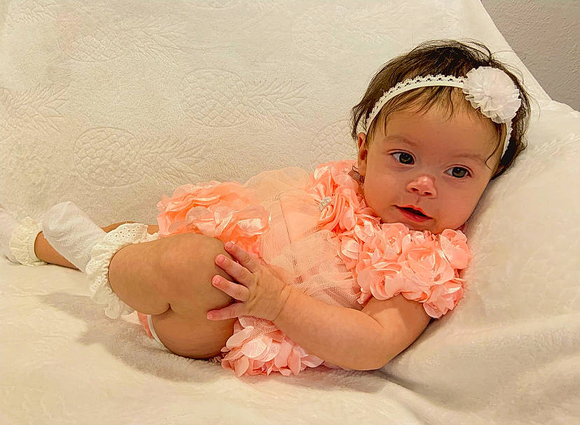 Azariah is registered to the contest to win money with this photo: baby, baby_toddler_clothing, cheek, comfort, dress, ear, embellishment, eye, eyelash, face, hair_accessory, happy, headband, headgear, headpiece, headwear, iris, peach, person, skin