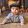 baby, child, crawling, hat, striped_shirt, floor, wooden_floor, fireplace, presents, gift_boxes, warm_lighting, indoors, holiday, cute, portrait, young_child, expression, home, cozy, decor