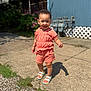 toddler, child, smiling, standing, outdoor, concrete, sunlight, coral_clothing, shorts, top, sandals, happy, face, person, greenery, blue_wall, utility_meters, fence, shadow, daylight