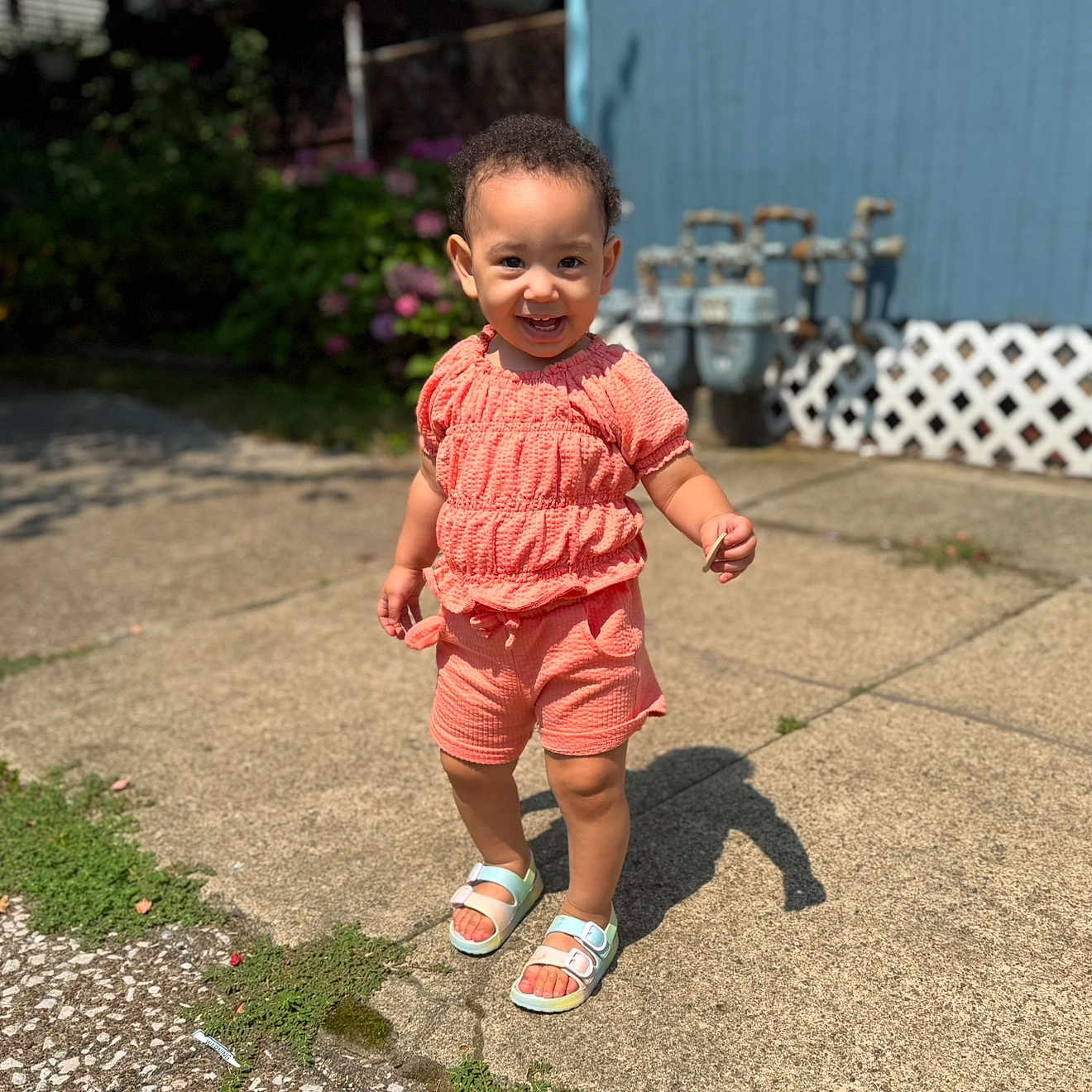 Miiamour joined the competition — help win amazing prizes! blue_wall, child, concrete, coral_clothing, daylight, face, fence, greenery, happy, outdoor, person, sandals, shadow, shorts, smiling, standing, sunlight, toddler, top, utility_meters