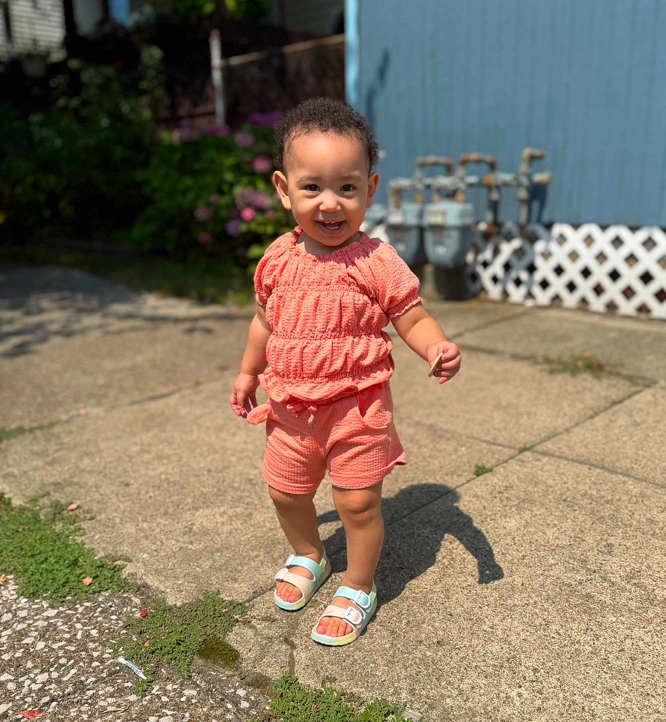 Miiamour joined the competition — help win amazing prizes! toddler, child, smiling, standing, outdoor, concrete, sunlight, coral_clothing, shorts, top, sandals, happy, face, person, greenery, blue_wall, utility_meters, fence, shadow, daylight
