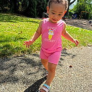 Miiamour is registered to the contest to win money with this photo: toddler, child, pink_outfit, sandals, walking, outdoor, park, playground, grass, sunlight, shadow, curly_hair, summer, happy, smiling, nature, trees, path, casual_clothing, daytime