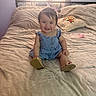 baby, child, smiling, denim_dress, pink_bow, baby_bottle, pillow, tiger_design, bed, blanket, sunlight, window, curtains, indoor, footwear, sandals, happy, person, portrait, cute