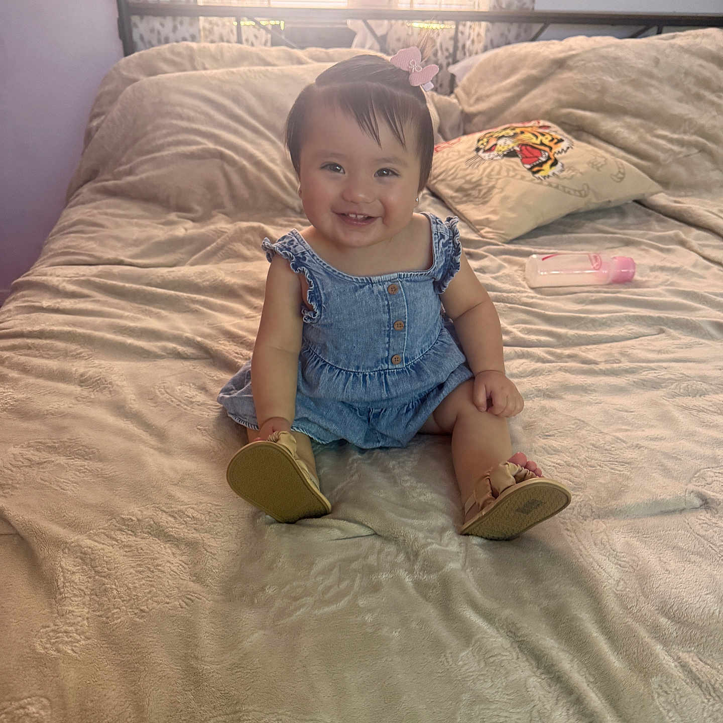 Valeria is registered to the contest to win money with this photo: baby, child, smiling, denim_dress, pink_bow, baby_bottle, pillow, tiger_design, bed, blanket, sunlight, window, curtains, indoor, footwear, sandals, happy, person, portrait, cute