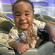 Damiree joined the competition — help win amazing prizes! baby, child, smiling, happy, portrait, stroller, indoor, playground, amusement_park, colorful, curly_hair, infant, sitting, front_facing, casual_clothing, bib, toy_print, family_outing, close_up, photography