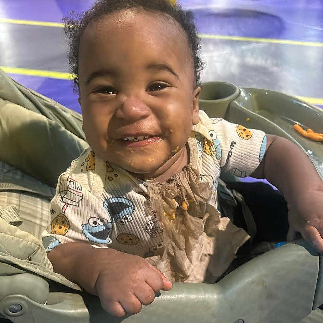 Damiree joined the competition — help win amazing prizes! baby, child, smiling, happy, portrait, stroller, indoor, playground, amusement_park, colorful, curly_hair, infant, sitting, front_facing, casual_clothing, bib, toy_print, family_outing, close_up, photography