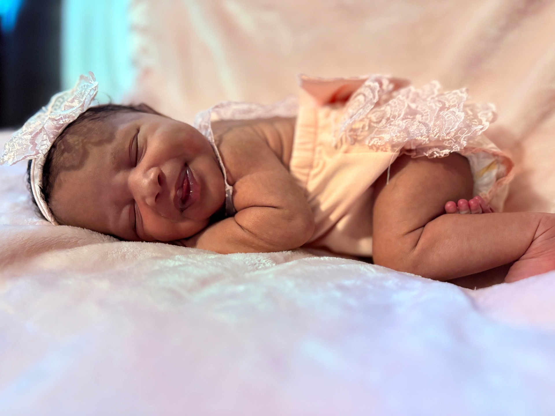 Aurora is registered to the contest to win money with this photo: baby, sleeping, infant, pink_outfit, lace, headband, smile, blanket, soft_texture, cute, newborn, peaceful, resting, child, portrait, indoors, closeup, skin, legs, arm